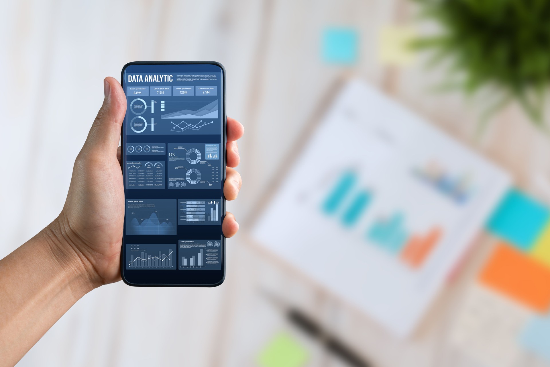 Hand Holding Smartphone Displaying Data Analytics in Modern Workspace. Agnostic